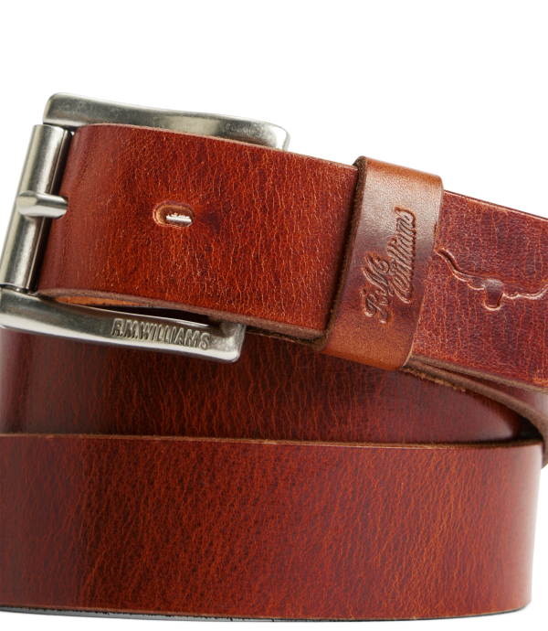 A close-up of a brown leather belt with a silver-tone buckle, showing the textured leather, a keeper loop embossed with 'St. Louis', and 'STANLEY RARROE' engraved on the buckle.