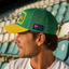 FIFA World Cup Australia Cap - Green. Man wearing a green and yellow cap with a logo in an outdoor setting.