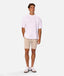 A man modeling a light pink short-sleeve t-shirt, beige drawstring shorts, and white sneakers against a solid light gray background.