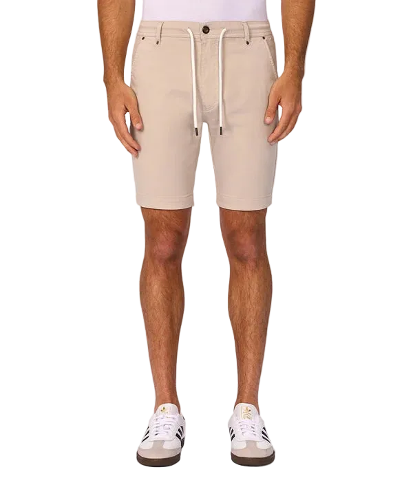 A person wearing light beige drawstring shorts, shown from the waist down against a plain light gray studio background. The shorts have a white drawstring and are paired with white sneakers.