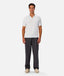 A man modeling a white short-sleeve polo shirt paired with dark gray trousers and beige sneakers, standing against a light gray studio background.