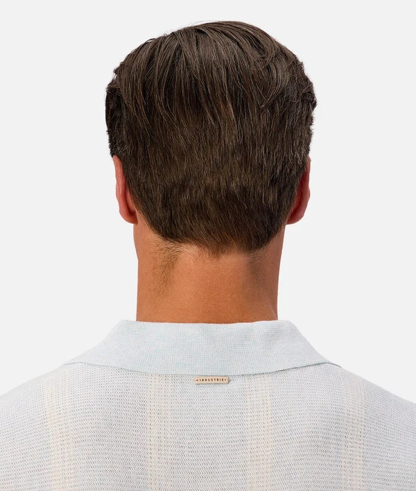 Back view of a man wearing a light blue knit polo shirt, showing the collar and a small 'INDUSTRIE' brand tag.