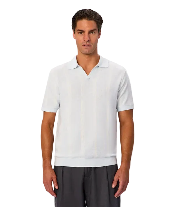 A man wearing a light blue short-sleeve knit polo shirt with subtle vertical stripes, paired with dark gray trousers, against a plain light gray background.