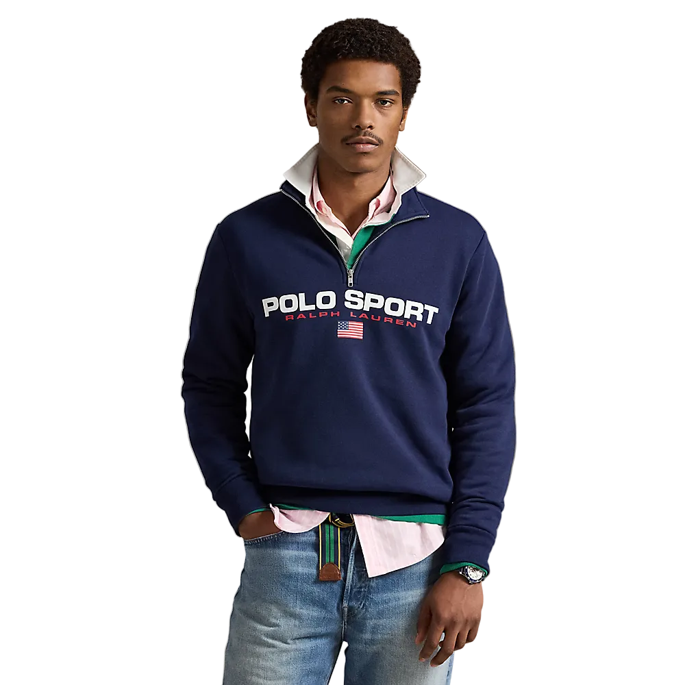 A man wearing a navy blue Polo Ralph Lauren quarter-zip sweatshirt with a white and red striped shirt underneath, paired with blue jeans, standing against a neutral beige background.