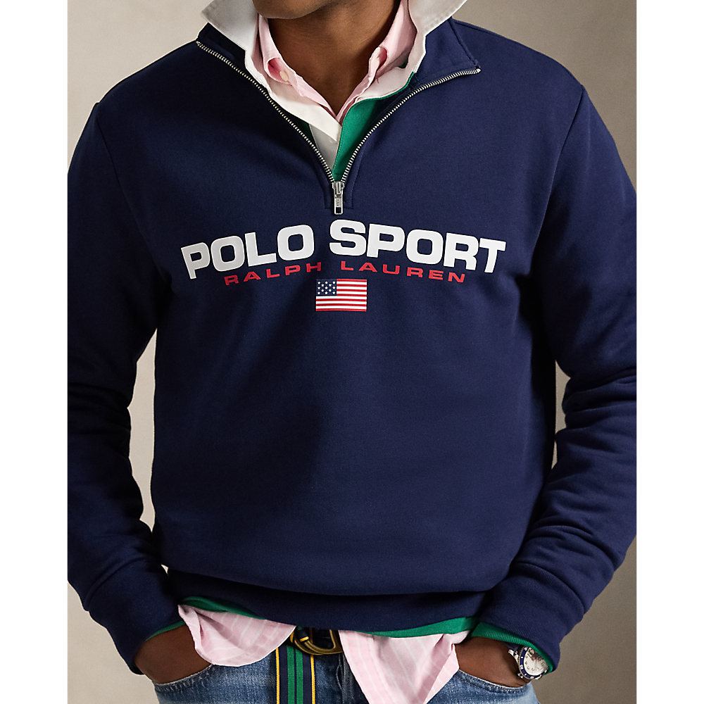 A man wearing a navy blue Polo Ralph Lauren quarter-zip sweatshirt over a pink collared shirt and green undershirt, paired with blue jeans.