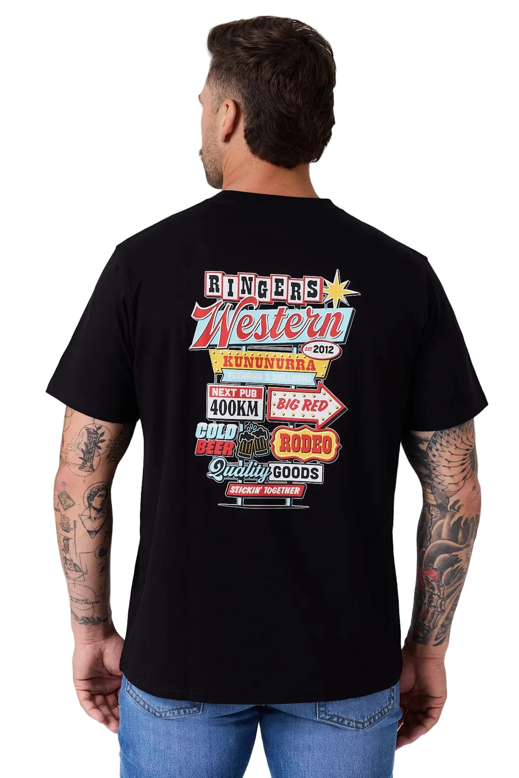 A man wearing a black t-shirt, viewed from the back. The shirt features a large, colorful graphic print on the back with western-themed text and logos, including 'Riders Western' and '2012'.