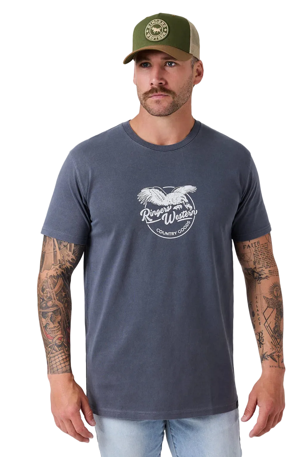 A man wearing a dark slate blue t-shirt with a white graphic print of an eagle and the words 'Ranger Wear Country Club'. He is also wearing an olive green trucker hat and light wash jeans, standing against a light gray studio background.