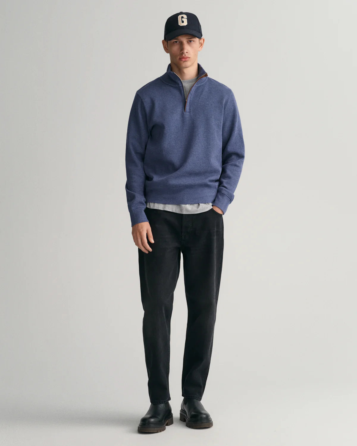 GANT - Sacker Rib Half-Zip Sweatshirt - Dark Jeans-Blue Melange worn with black pants and cap, showcasing a smart-casual look.