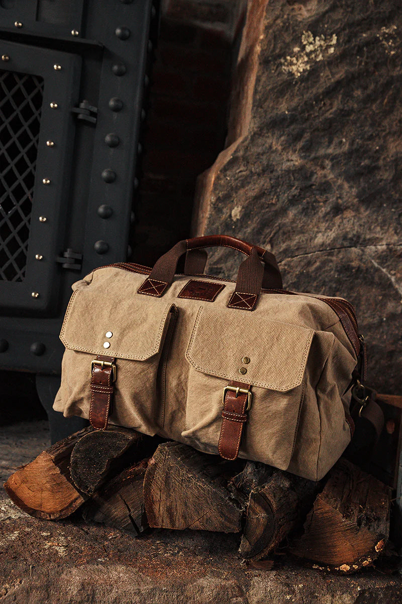 Ringers Western - Waxicanvas Duffle Bag - Sand resting on wood, showcasing durable design and leather accents.