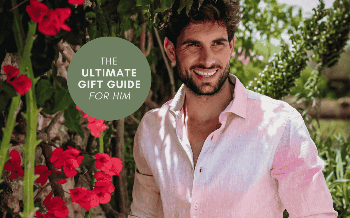 A smiling man in a light shirt surrounded by flowers, featured in The Ultimate Gift Guide For Him.