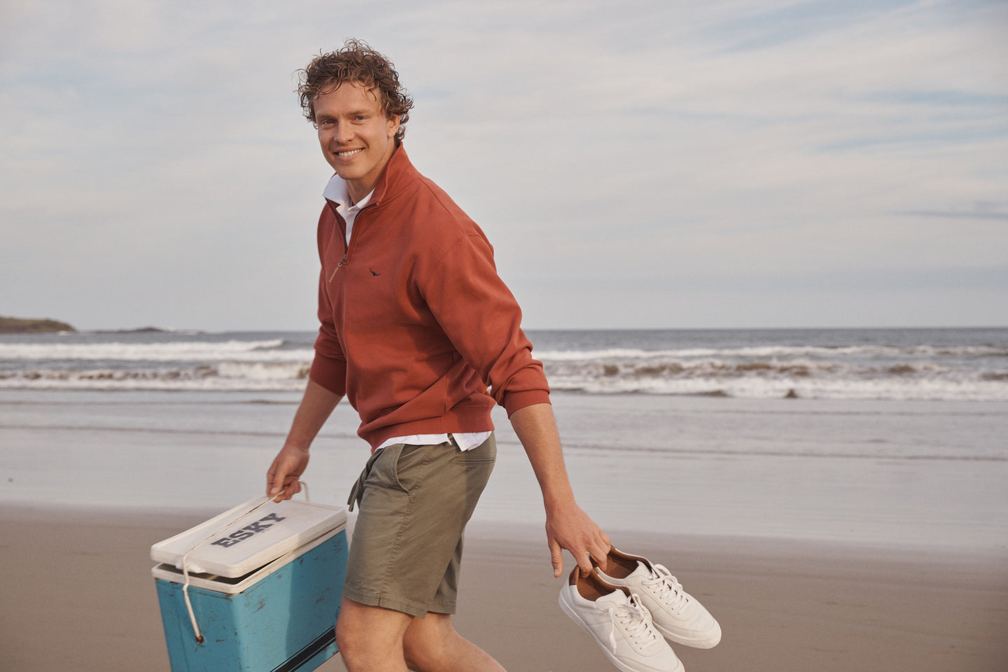 Summer Style Picks for Men: 2025 Summer Essentials featuring a stylish man on the beach with a cooler.