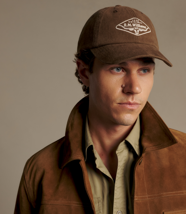 A man wearing a brown baseball cap with a white embroidered logo that reads 'R.M.