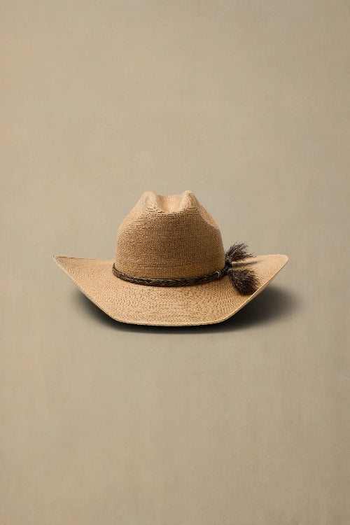 A light tan woven cowboy hat with a dark brown braided band and a feather accent on the side, displayed against a solid beige background.