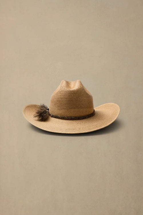 A light tan woven cowboy hat with a dark brown band and a small dark feather accent on the left side, displayed against a solid beige background.
