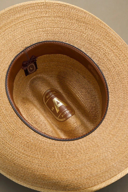Close-up top-down view of a woven straw cowboy hat showing the tan interior, dark brown inner band, and a gold-toned brand tag inside the crown.