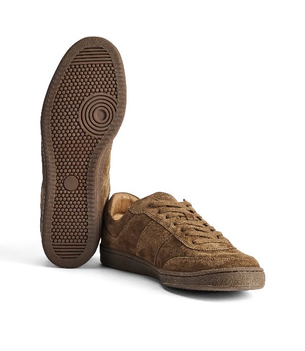 A pair of brown suede low-top sneakers, with one shoe standing upright to show the textured outsole and the other lying flat to show the side profile, on a clean white background.