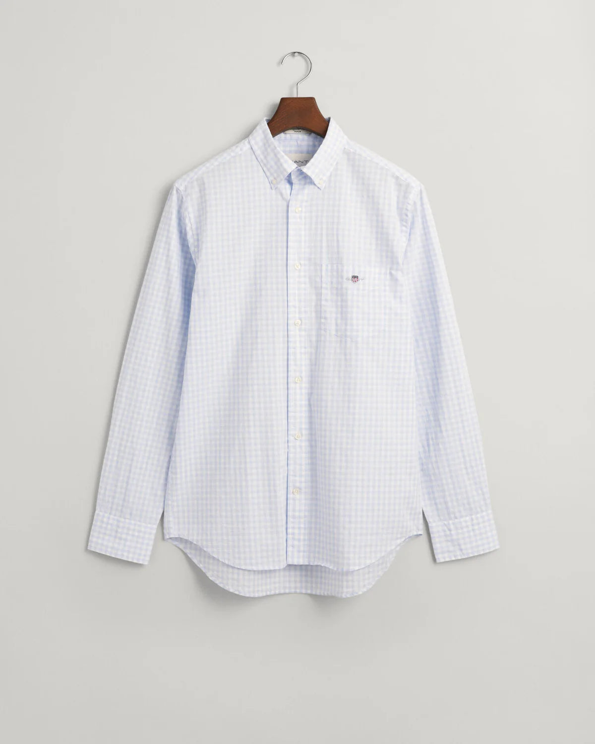 GANT - Poplin Shirt - Gingham - Light Blue & White hanging on a hook, showcasing its button-down collar and chest pocket.
