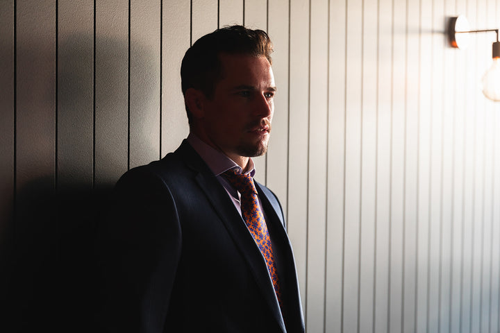 Orange store promotional image featuring a man in a suit standing against a wood-panel wall.