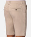 Close-up back view of a person wearing beige chino shorts with a buttoned welt pocket, waistband belt loops, and side pockets, against a light gray studio background.