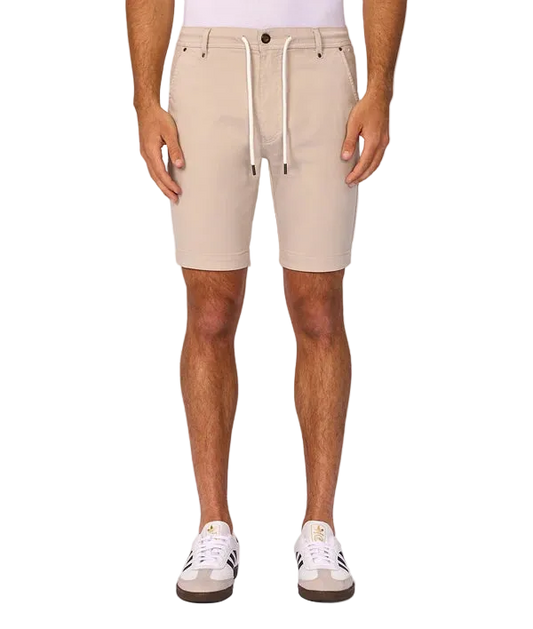 A person wearing light beige drawstring shorts, shown from the waist down against a plain light gray studio background. The shorts have a white drawstring and are paired with white sneakers.