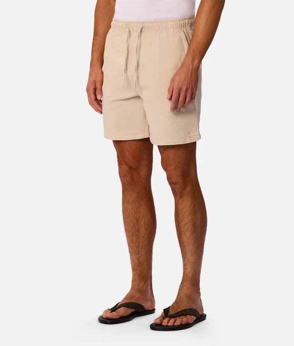 Beige drawstring shorts worn by a model, paired with black flip-flops, shown from the waist down on a light gray background.