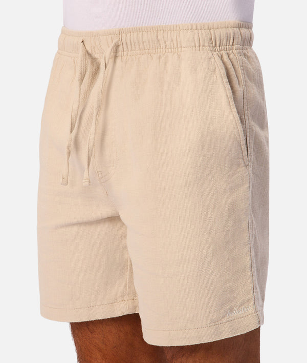 Beige drawstring shorts with a textured linen-like fabric, shown on a model from the waist down against a light gray background.