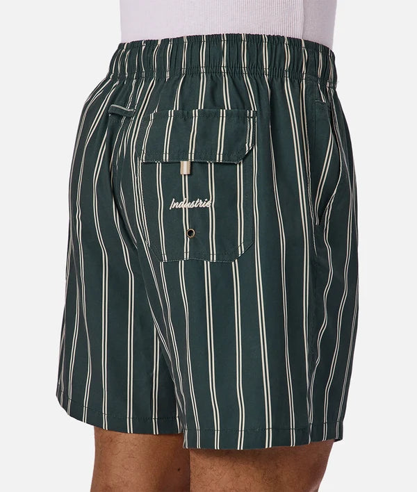A close-up of a person wearing dark green and cream vertically striped shorts with a side pocket featuring the brand name 'Industrial' embroidered on it.