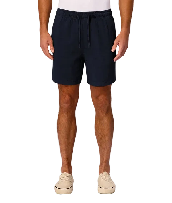 A man wearing dark navy blue drawstring shorts, paired with a white t-shirt and beige platform sneakers, standing against a light gray studio background.