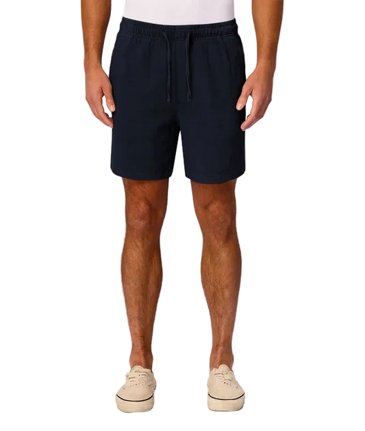 A man wearing dark navy blue drawstring shorts, paired with a white t-shirt and beige platform sneakers, standing against a light gray studio background.