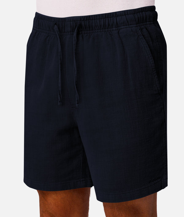 A close-up of a person wearing dark navy drawstring shorts, showing the waistband, fabric texture, and side pockets against a light gray background.