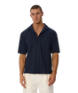 A man wearing a dark navy blue short-sleeve button-up shirt with a chest pocket, paired with off-white pants, standing against a light gray background.