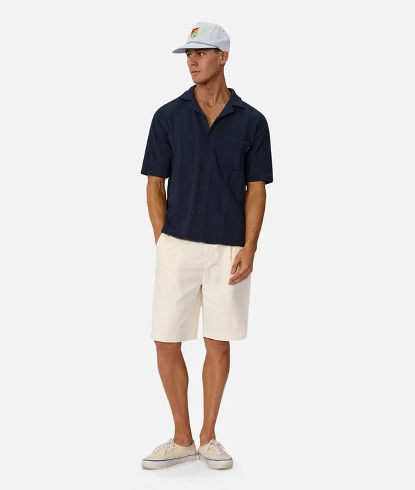 Man wearing a navy polo shirt, white shorts, and a white cap on a white background