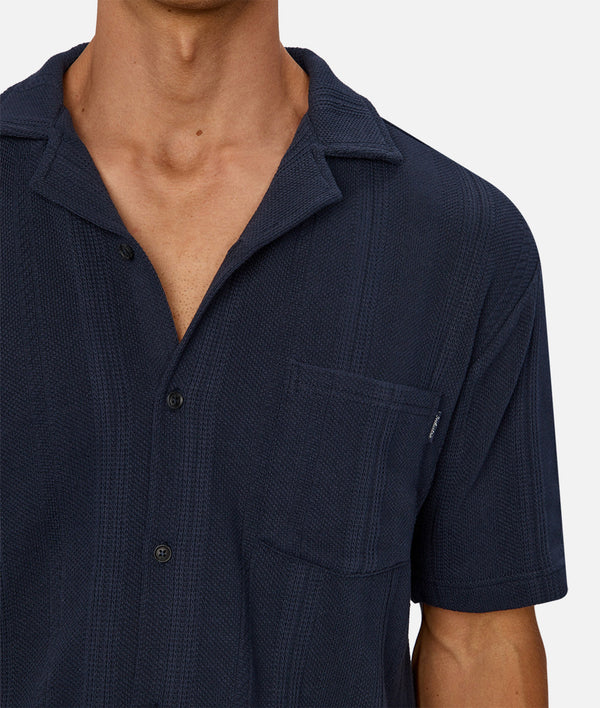 Navy blue short-sleeve shirt worn by a person on a white background