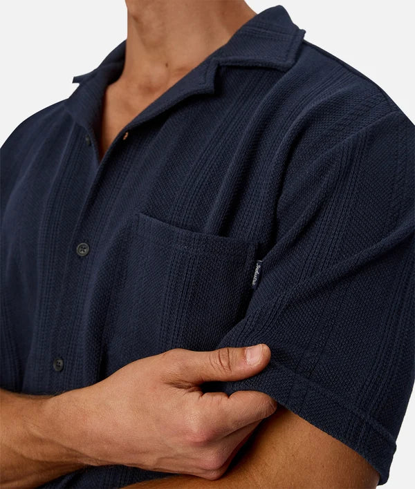 Close-up of a man wearing a navy blue short-sleeve button-up shirt with a textured waffle-weave pattern and a chest pocket.