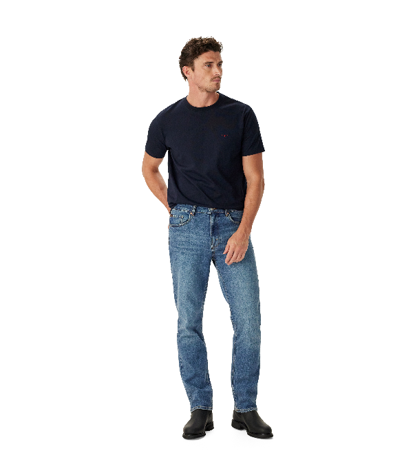 A man wearing a dark navy blue crewneck t-shirt and light blue jeans, standing against a solid white background.