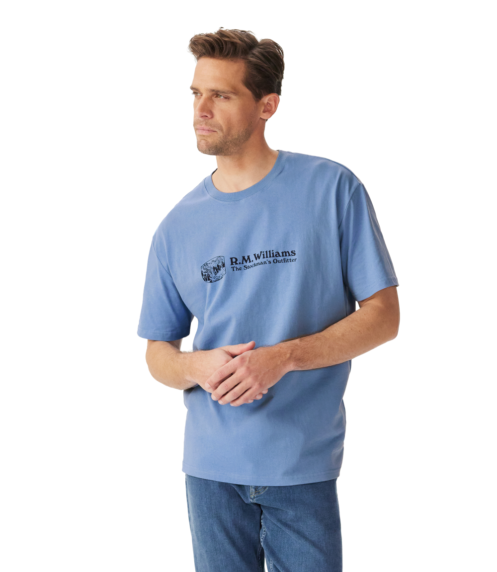 R.M.Williams - Outfitter T-Shirt - Soft Blue worn by a model, showcasing the crew neck and branded print.