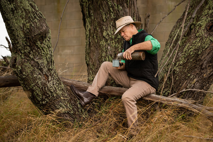 Dubbo store promotional image featuring a man in outdoor clothing pouring a drink while seated on a fallen tree.