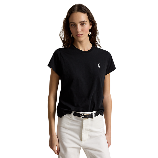 A woman modeling a black short-sleeve crewneck t-shirt with a small white embroidered polo player logo on the left chest, paired with white pants and a black belt, against a plain white background.