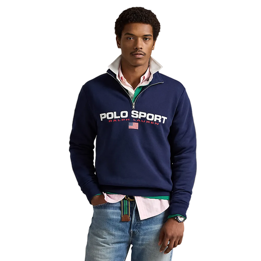 A man wearing a navy blue Polo Ralph Lauren quarter-zip sweatshirt with a white and red striped shirt underneath, paired with blue jeans, standing against a neutral beige background.