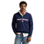 A man wearing a navy blue Polo Ralph Lauren quarter-zip sweatshirt with a white and red striped shirt underneath, paired with blue jeans, standing against a neutral beige background.