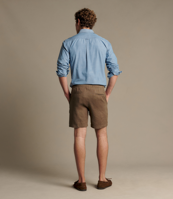 Man wearing brown linen shorts with a blue button up shirt. 