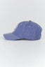 A blue denim baseball cap with a curved brim, featuring a white embroidered logo on the side and orange eyelets, photographed on a light gray background.