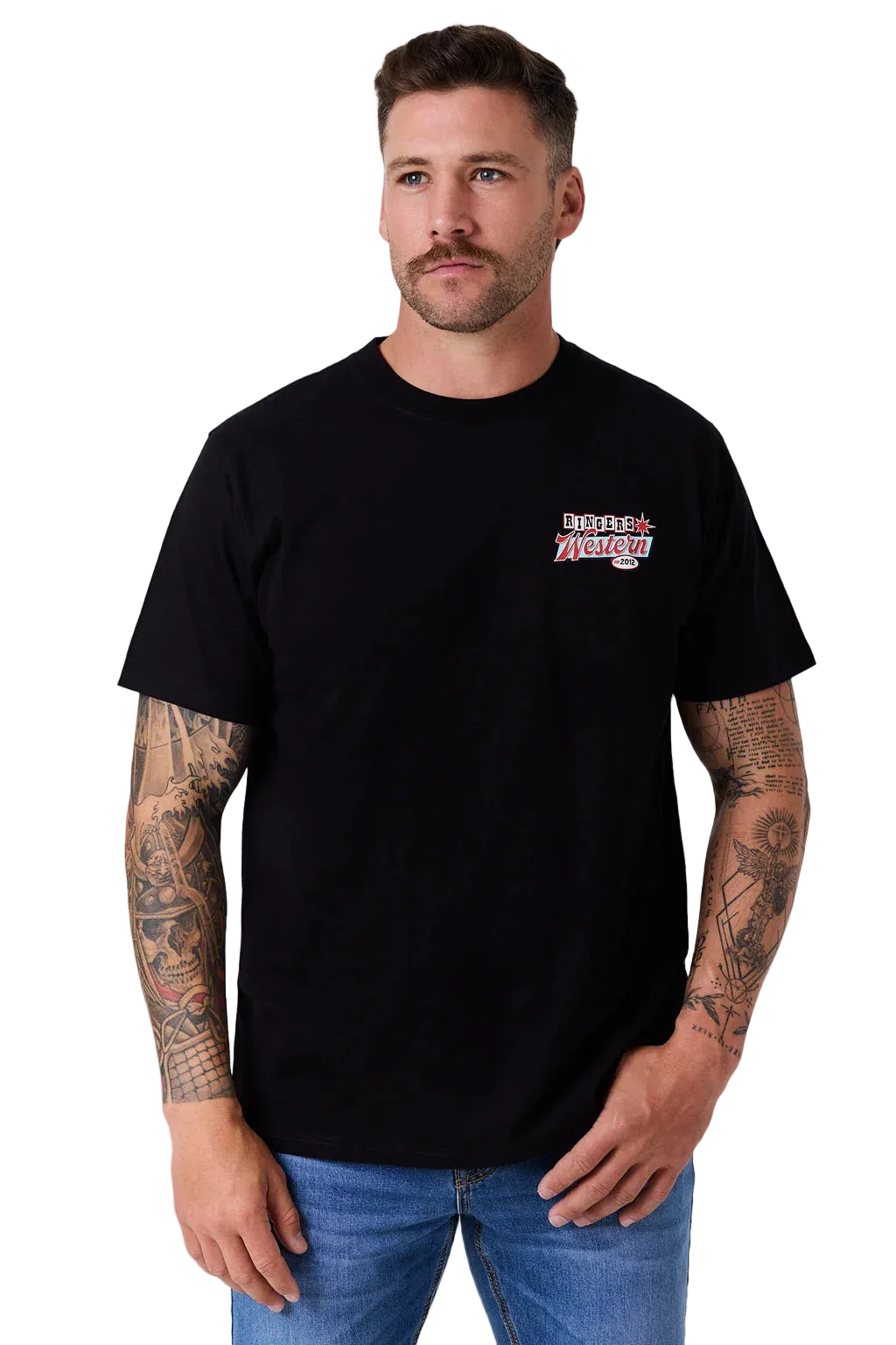 A man wearing a black short-sleeve t-shirt with a small red, white, and blue graphic on the left chest, paired with blue jeans, against a light gray studio background.
