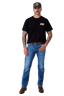 A man modeling a black short-sleeve t-shirt with a small red and white graphic on the left chest, paired with blue jeans, a brown belt, and brown boots, standing against a light gray studio background.