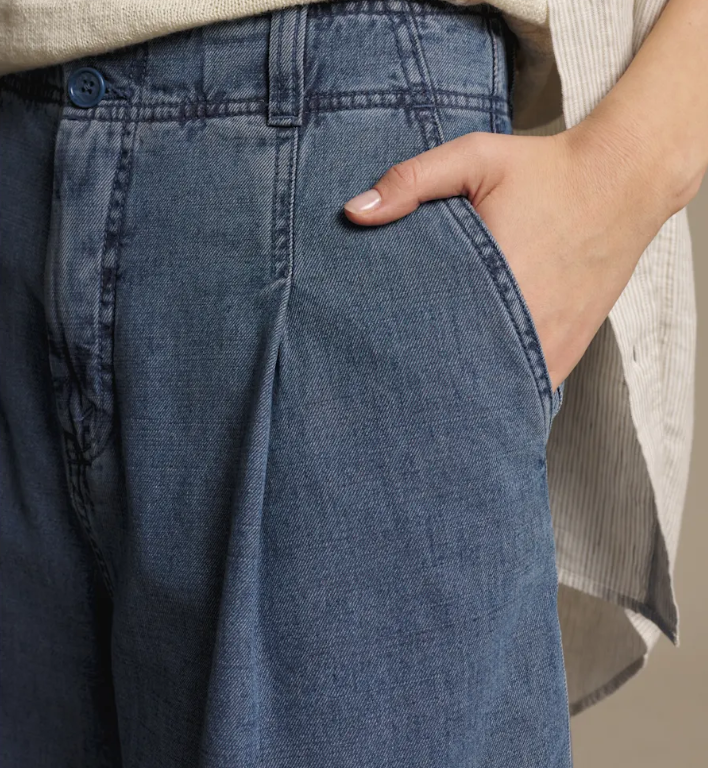 Close-up of a person wearing wide-leg blue denim pants, with a hand resting in the pocket and part of a light-colored striped top visible.