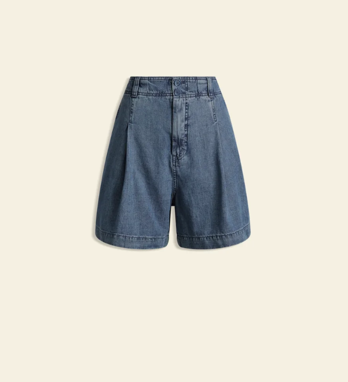 A pair of high-waisted blue denim shorts with pleated front details, shown flat against a solid light beige background.
