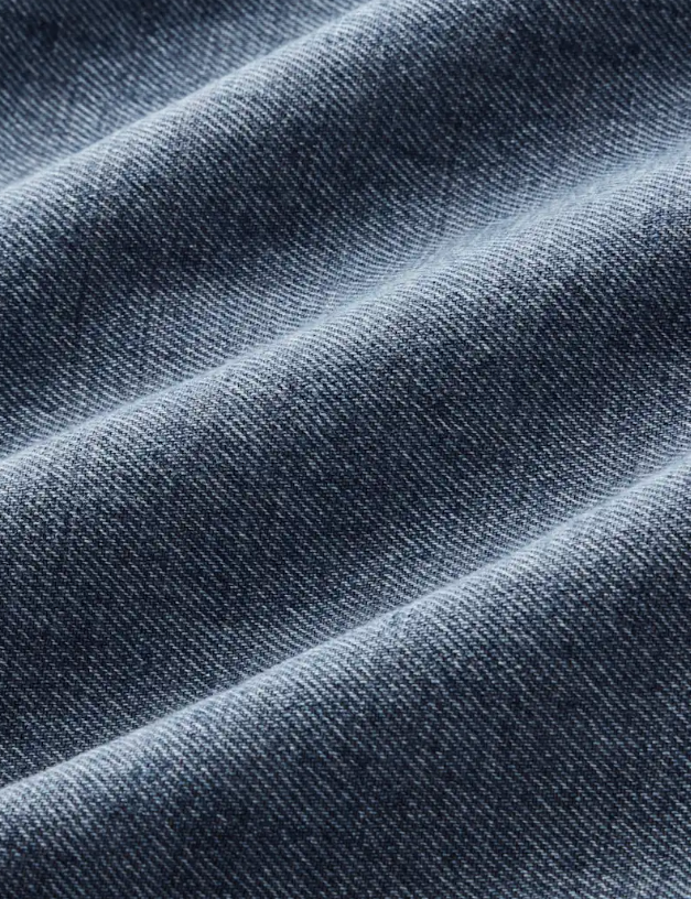 A close-up of dark blue denim fabric with a visible twill weave and soft diagonal folds.