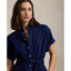 Woman wearing a blue Linen shirt dress, short sleeve, holding a straw bag - Polo Ralph Lauren - Belted Short-Sleeved Linen Shirt Dress - Newport Navy