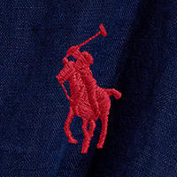 Woman wearing a blue Linen shirt dress, short sleeve, holding a straw bag - Polo Ralph Lauren - Belted Short-Sleeved Linen Shirt Dress - Newport Navy
